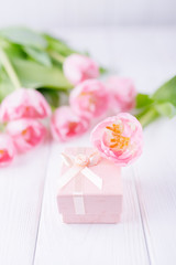 Beautiful pink tulips and pink gift box on a white wooden background. Free space