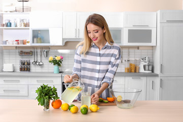 Young woman pouring lemonade into mason jar on table in kitchen. Natural detox drink