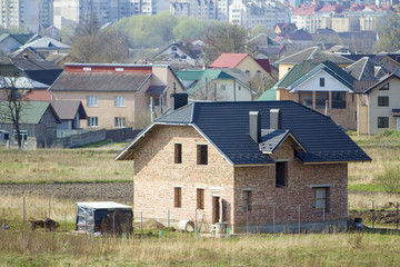 Brand new spacious brick two story residential house with tiling roof and windows openings in suburban neighborhood on background of distant city.Building, mortgage and rel estate property.