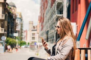 Happy young woman sitting at outdoor and using her cellphone.