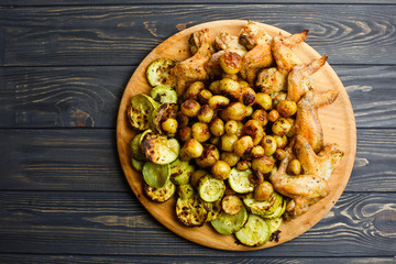 Grilled vegetables and chicken wings on the wooden plate. Free space.