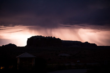Silhouette of canyons in Utah in front of rainy thunderstorm with lightening