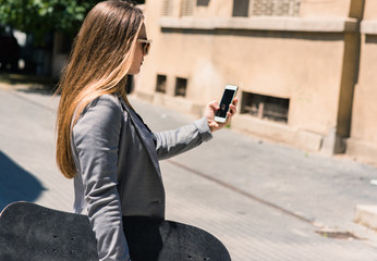 Walking business girl holding a skateboard and watching in cellphone