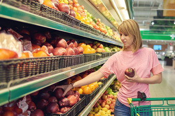 Slender Caucasian woman choosing apples during shopping at supermarket.