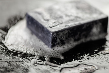 block of natural carbon charcoal soap on black stone background with bubbles - 207538481