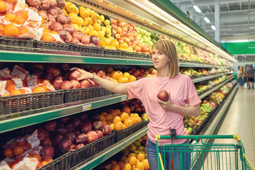 Slender woman standing in front of a row of fruits in a grocery store.