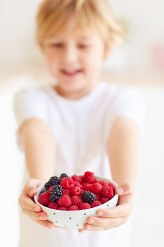 young boy, kid holding a plate of fresh and ripe raspberries and blackberries