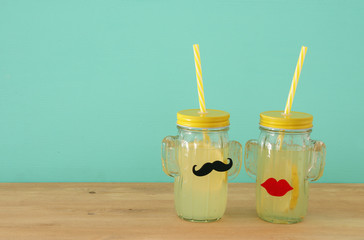 Image of fresh lemonade drink in cute cactus shape glasses wearing mustache and lips, over wooden table. Tropical summer romantic vacation concept.