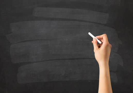 Female hand holding white chalk in front of a blank blackboard