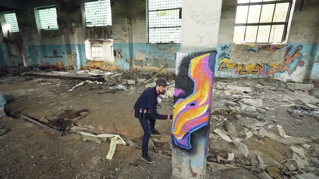 High angle shot of young urban painter creating abstract image on column in old damaged building. Modern art, street artist, creativity and people concept.
