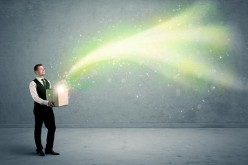 Fototapeta premium Bright yellow, green light beams escaping a cardboard box held by young elegant male business person in stylish suit concept.