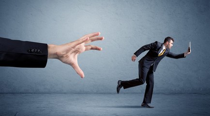 Young miniature businessman running from a big hand with blue background