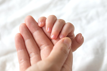 Baby uses his tiny fingers to hold his mother's finger to make him feeling her love, warm, comfort and secure.