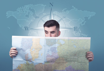 Handsome young man holding a map with a world map and a compass behind him