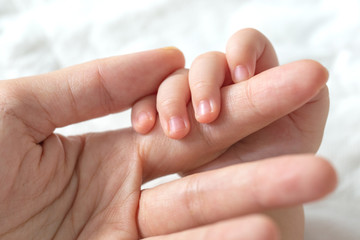 Baby uses his tiny fingers to hold his mother's finger to make him feeling her love, warm, comfort and secure.
