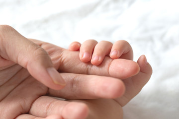Obraz na płótnie Canvas Baby uses his tiny fingers to hold his mother's finger to make him feeling her love, warm, comfort and secure.
