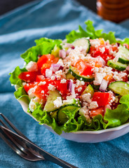 vitamin salad with tomato, cucumber, onion, lettucce and cottage cheese in white bowl on table