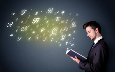 Casual young man holding book with shiny letters flying out of it