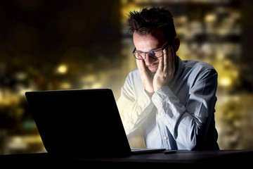 Young handsome businessman working late at night in the office with city lights in the background