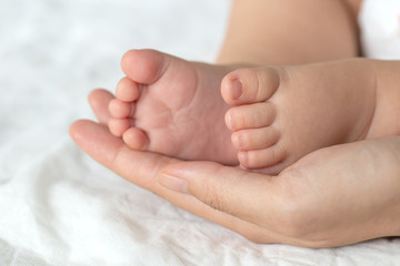 Mother uses her hand to hold her baby's tiny feet to make him feeling her love, warm, comfort and secure.