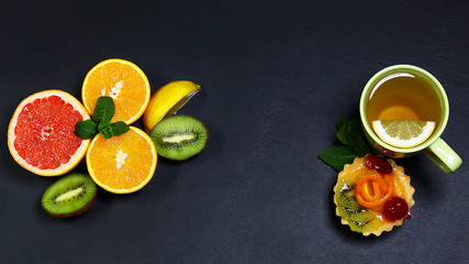 Variety of fruits grapefruit, oranges, kiwi, lemon, mint, cake, sweet fruit dessert bunched, cup of tea together on a shale board, the concept of healthy eating, copy space, top view set