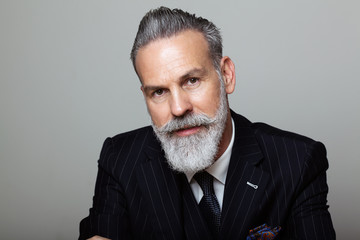 Portrait of attractive bearded gentleman wearing trendy suit over empty gray background. Studio shot, fashion concept.
