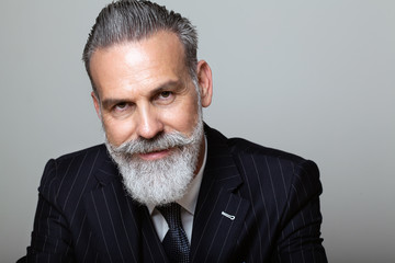 Portrait of attractive middle aged bearded gentleman wearing trendy suit over empty gray background. Studio shot, business fashion concept.