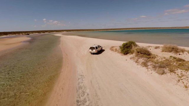 An aerial shot of a coast and sea with a ute driving on lands