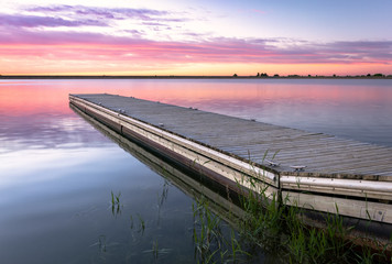 Sunrise or sunset on a fishing dock with colorful clouds reflecting in the lake