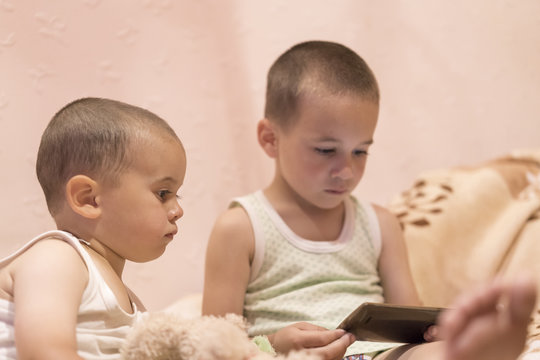 children in the bedroom watching cartoons. children play on smarfone. two brothers in the bedroom look at the smartphone.