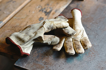 Old working gloves over wooden table, on a metal woodworking machine construction tools, gloves for...