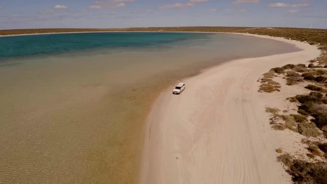 An aerial shot of a coast and sea with a ute driving on lands