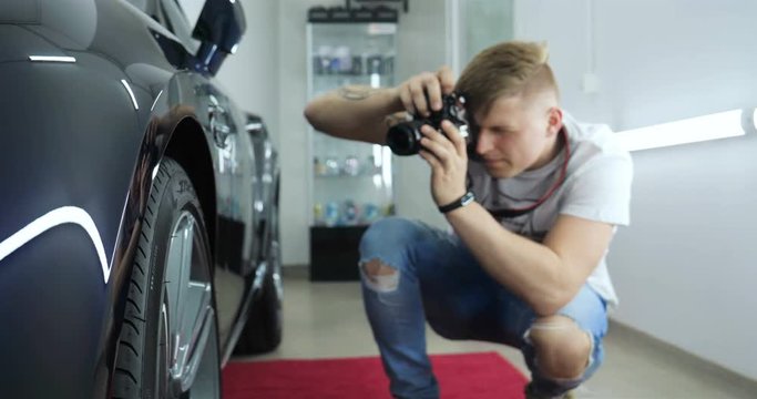 A young professional photographer (a guy, a man) takes pictures of a car in a car salon. Concept: lifestyle, new photo, car, photo camera, flash.