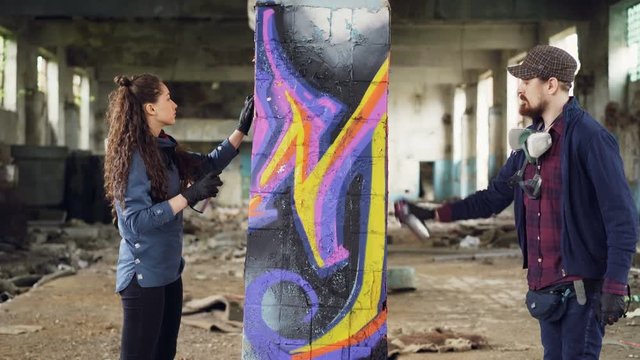 Two serious graffiti painters are decorating empty industrial building with abstract images using bright aerosol paint. Creative teamwork, young people and art concept.
