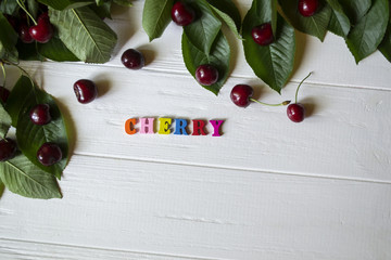 The branch with ripe cherries and multicolor letters on a white wooden table.