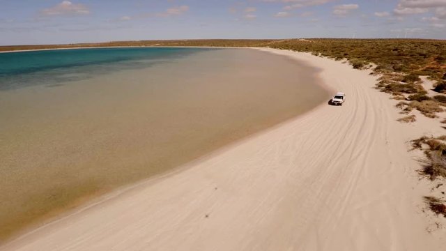 An aerial shot of a coast and sea with a ute driving on lands