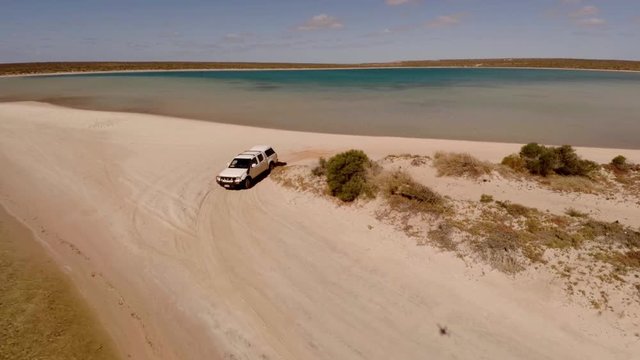 An aerial shot of a coast and sea with a ute driving on lands