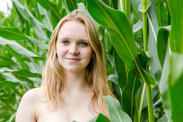 Eine junge hübsche Frau steht vor einem Maisfeld, sie ist sehr glücklich und lächelt