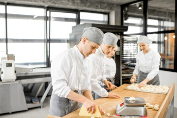 Group of young workers in uniform forming dough for baking on the wooden table standing together at the modern manufacturing