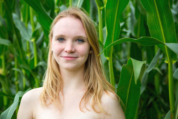 Fototapeta premium Eine junge hübsche Frau steht vor einem Maisfeld, sie ist sehr glücklich und lächelt
