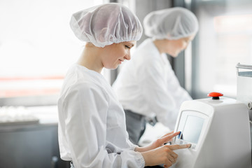 Women in uniform working with dough rolling machine at the bakery manufacturing