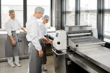 Bakers in uniform working with dough rolling machine making buns at the bakery manufacturing