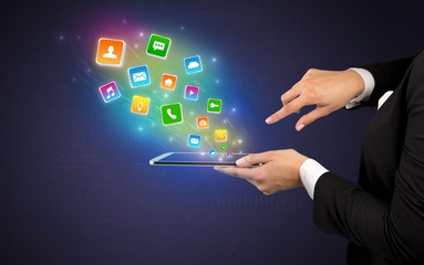 Hand holding tablet and application icons falling inwards
