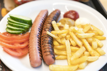 Grilled sausages with chips and vegetables on a white plate. harmful food concept