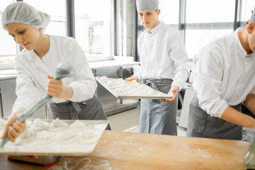 Group of young workers in uniform filling buns for baking on the wooden table standing together at the modern manufacturing