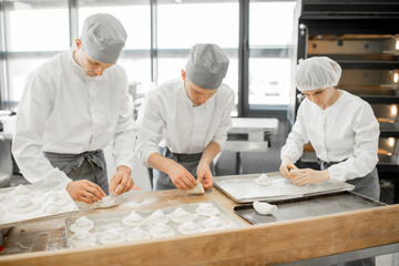 Group of young workers in uniform filling buns for baking on the wooden table standing together at the modern manufacturing