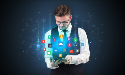 Fototapeta na wymiar Handsome businessman in suit with tablet on his hand and application icons above 