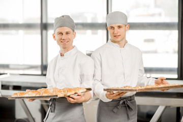 Portrait of a two bakers standing with tray full of freshly baked buns at the manufacturing