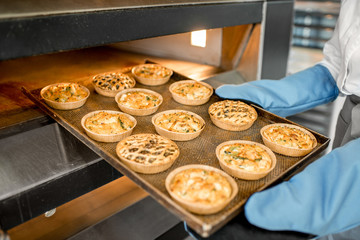Baker taking a tray with freshly baked buns from the oven at the manufacturing