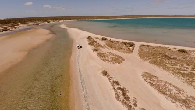 An aerial shot of a coast and sea with a ute driving on lands